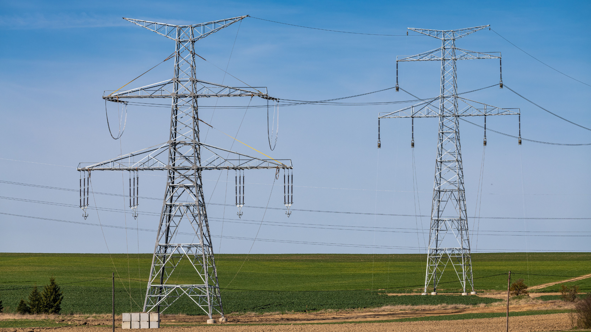 Scenic rural landscape featuring high voltage transmission towers under a clear blue sky.