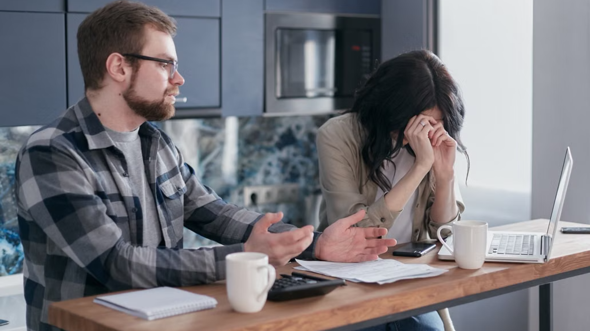 A young couple sits at their kitchen table reviewing bills and a shrinking budget, reflecting the financial squeeze facing many communities.
