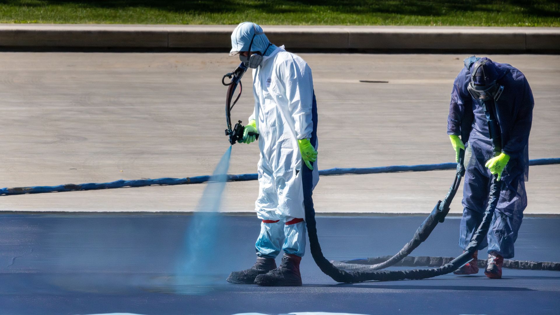Workers in protective suits spray-apply blue coating to the drained reflecting pool.