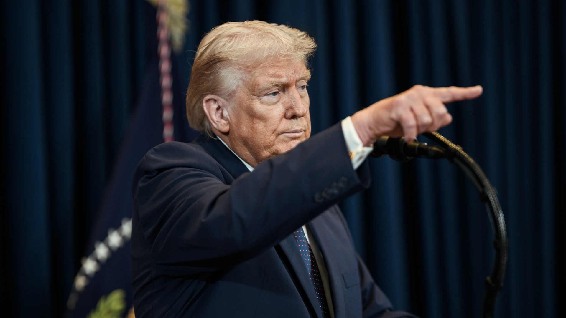 President Donald Trump gesturing while speaking at a podium microphone.