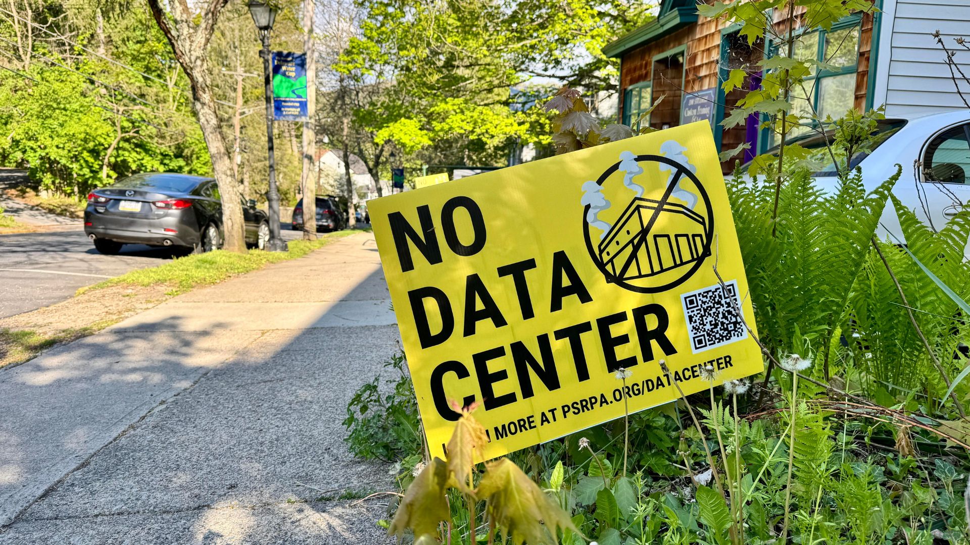 A yellow 'No Data Center' yard sign posted in a residential neighborhood garden.