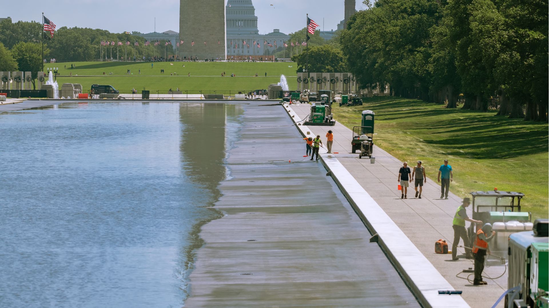 Workers maintaining the reflecting pool with the Washington Monument and Capitol in the background.
