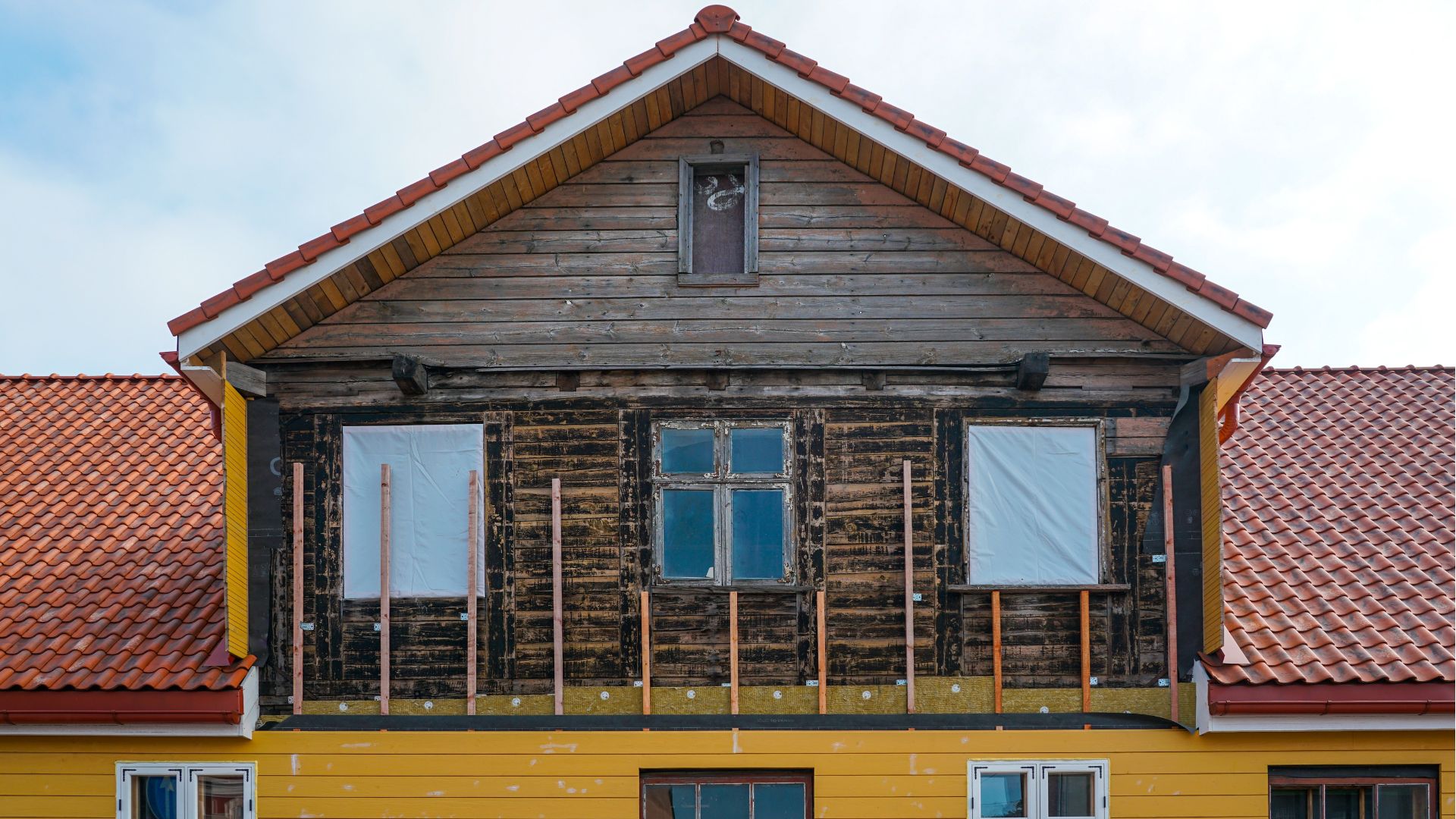 Front view of an old wooden house being restored with new siding, insulation, and roof upgrades during renovation.