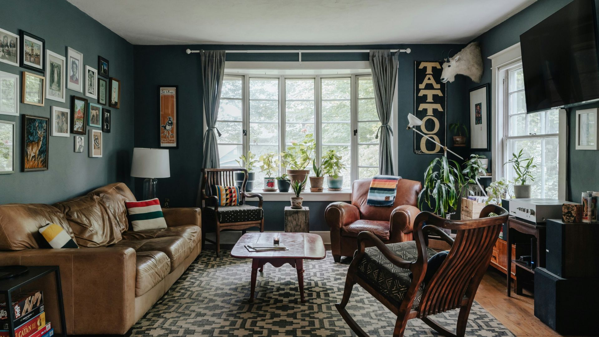 Cozy living room with leather seating, framed wall art, houseplants, and large windows.