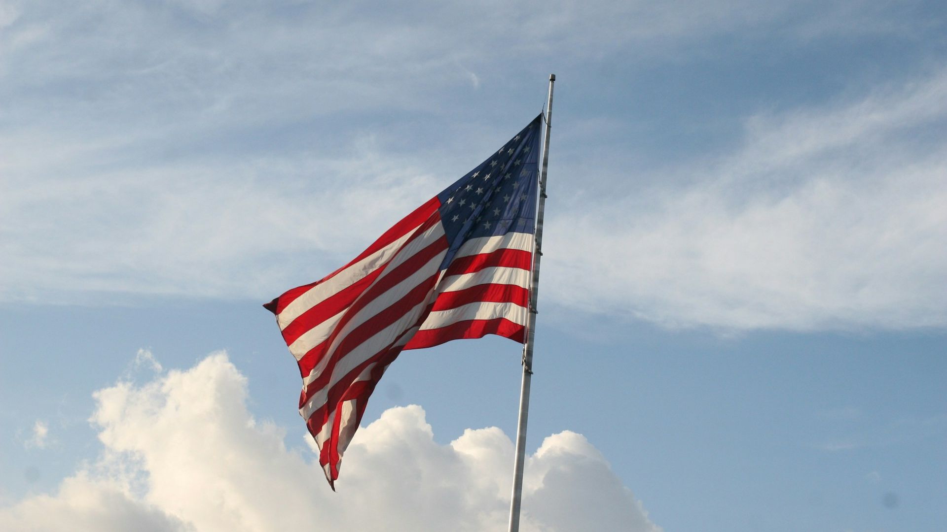 American flag waving against a partly cloudy blue sky.