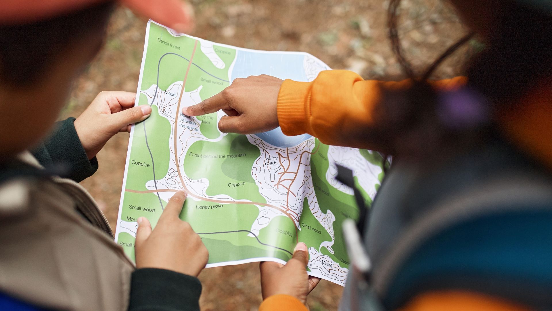 Hands holding a printed map while fingers point to locations on it outdoors. 