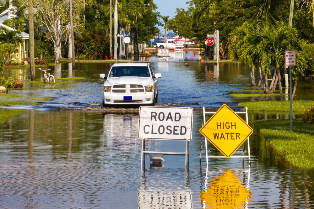 A truck drives through a street flooded by Hurricane Milton in Punta Gorda, Florida, near road closure and high water signs.