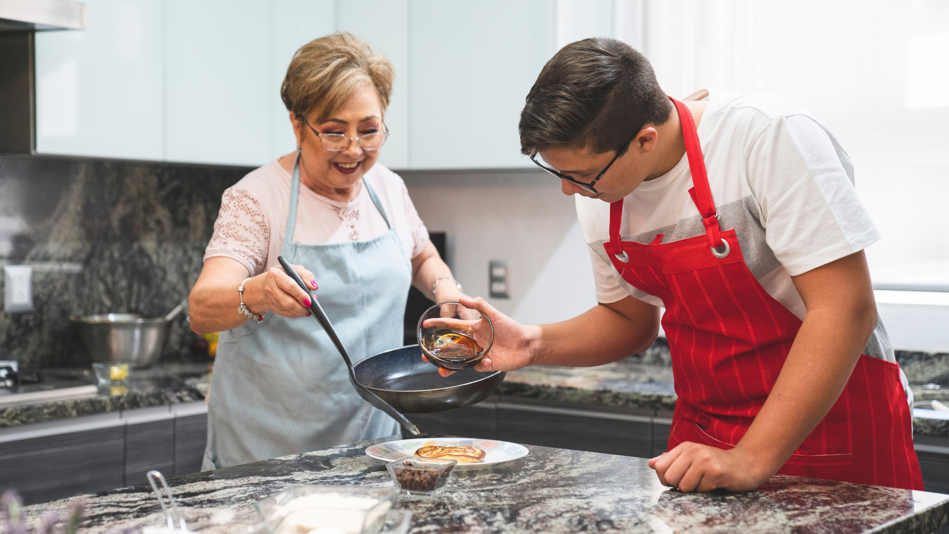 Elderly woman and young man cooking pancakes share a warm moment in a sunlit kitchen, symbolizing the unlikely roommate pairings reshaping how New Yorkers afford rent.