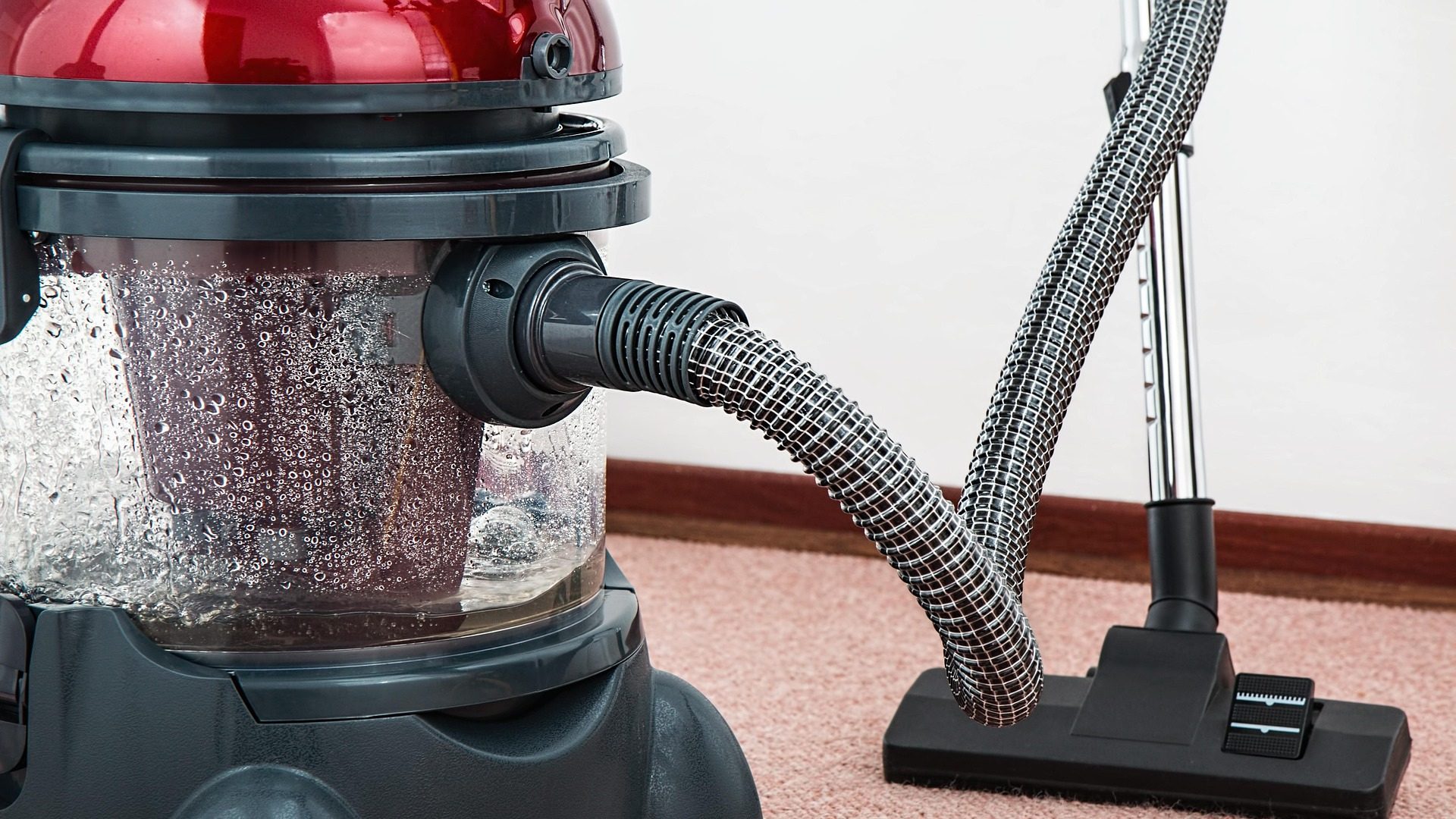 A vacuum cleaner positioned on a carpeted floor, ready for use in cleaning the surface.