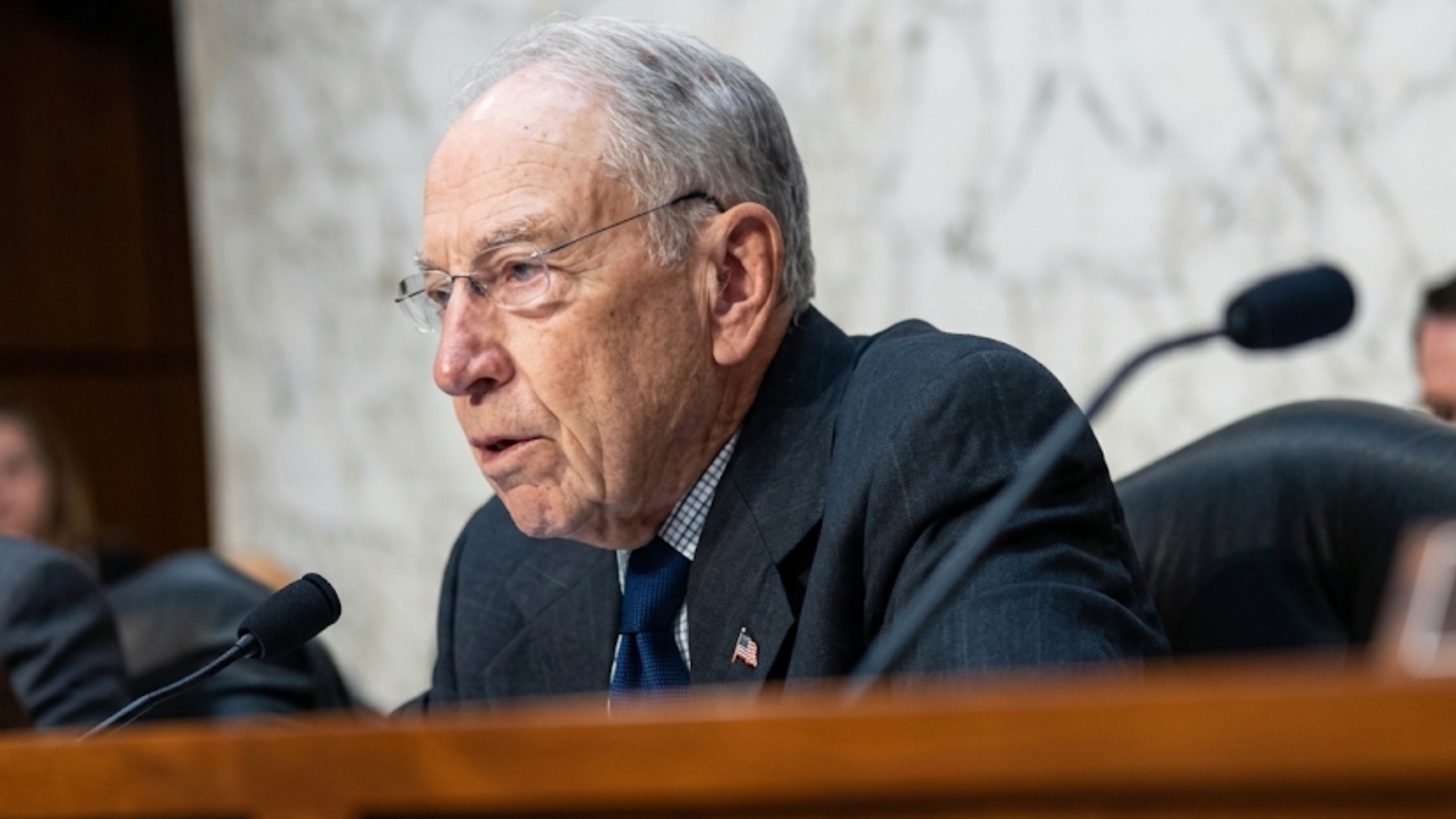Senator Chuck Grassley speaks seriously into a microphone at a formal hearing.