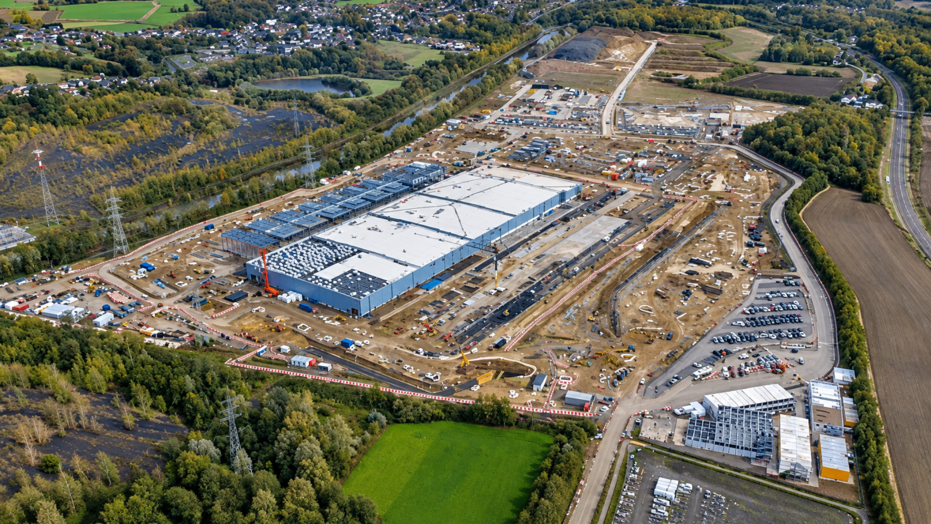 Aerial view of a large commercial construction site with a massive building complex and surrounding dirt plots.
