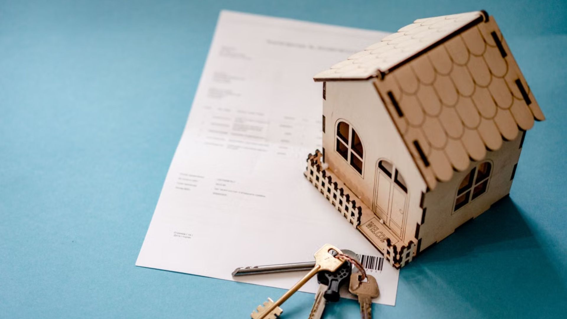 Model house and keys resting on mortgage paperwork against a blue background.