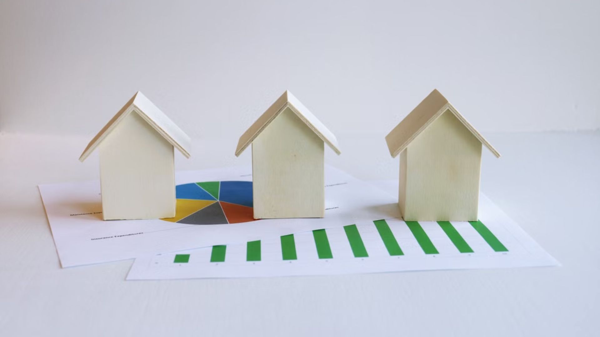 Three model houses positioned on charts illustrating housing and mortgage data.