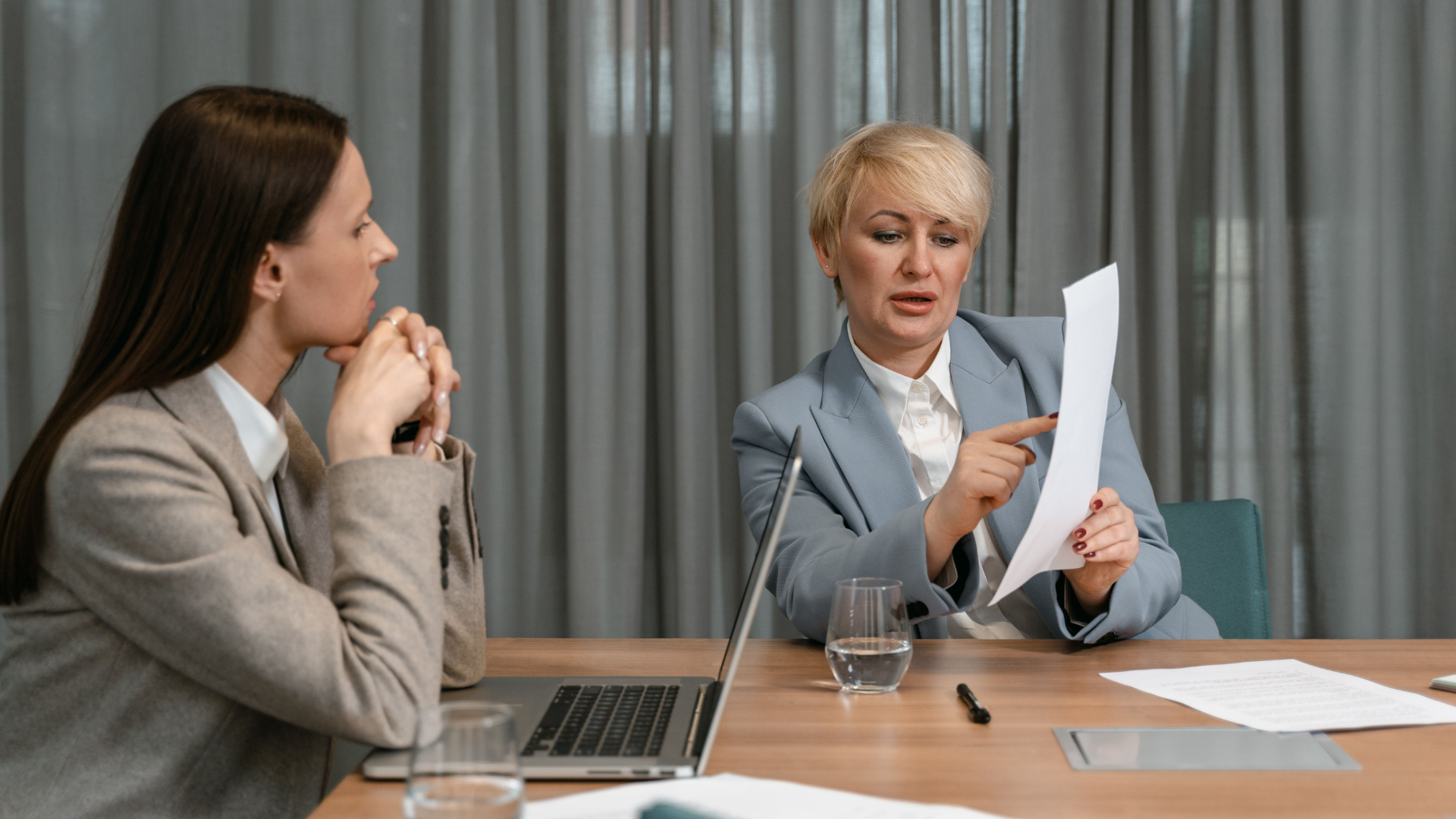 A financial planner reviews decades of benefit paperwork, discussing documents during a professional meeting around a conference table.