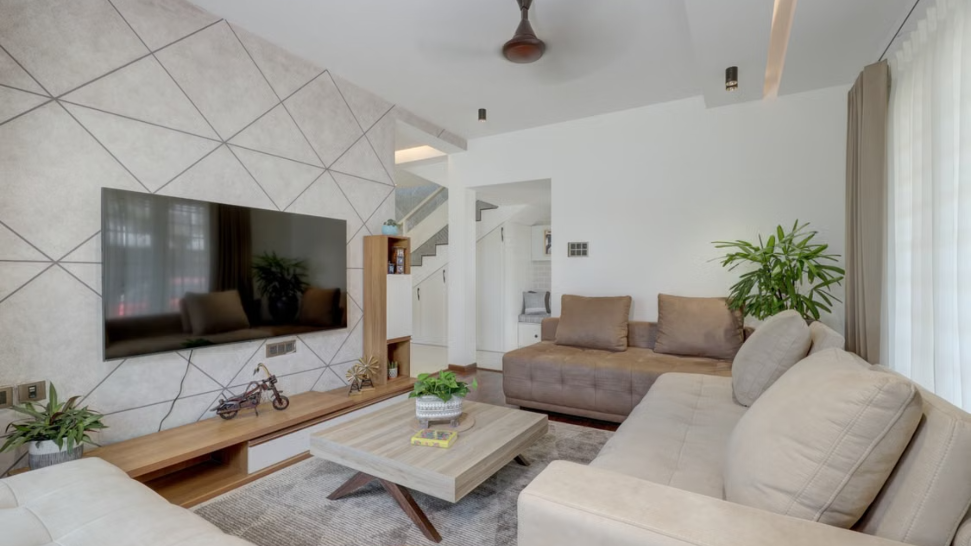 Modern living room with a flat-screen TV on a geometric accent wall, a brown sofa, and a wooden coffee table.