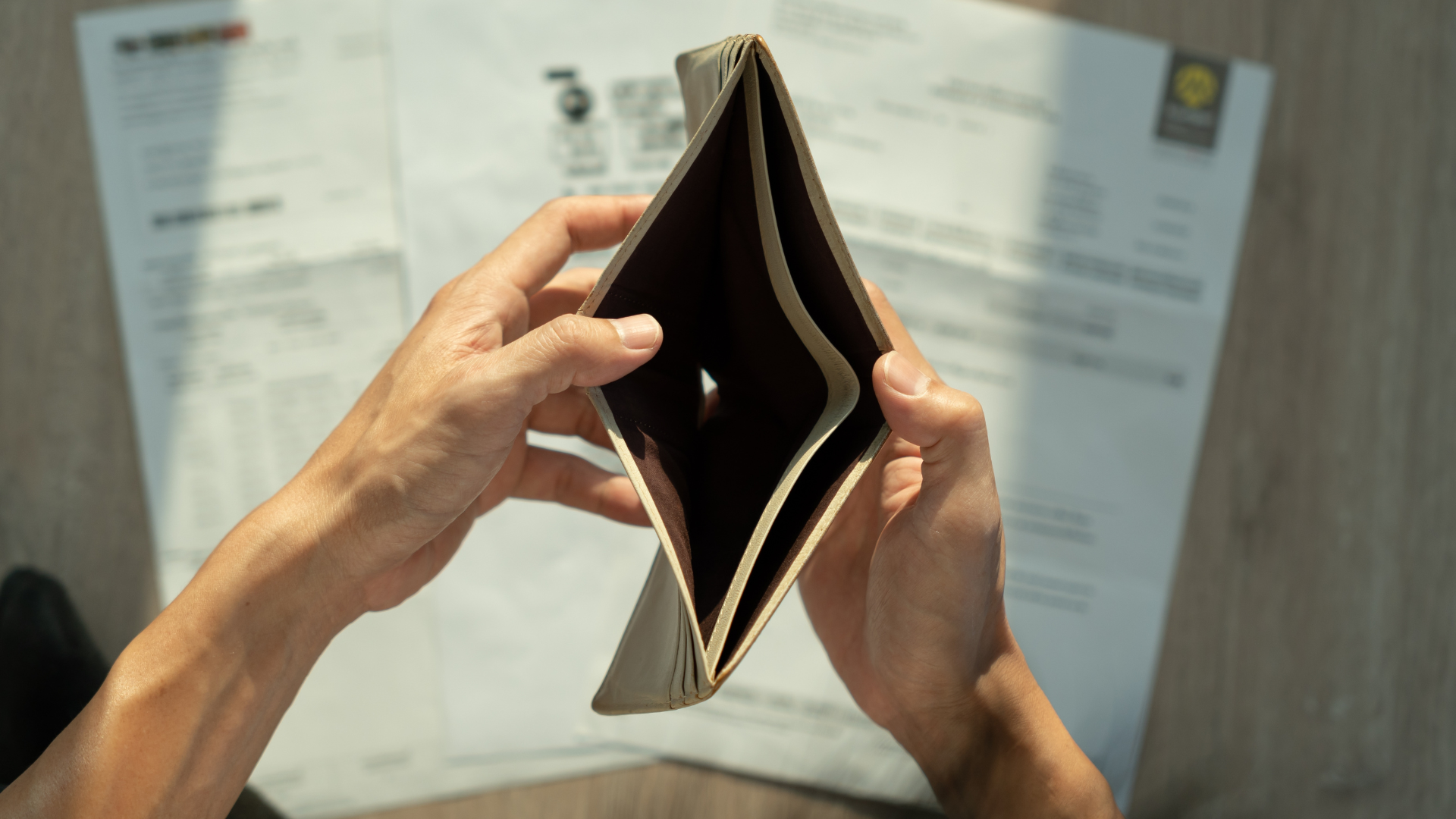 Hands opening an empty brown wallet over paper bills.
