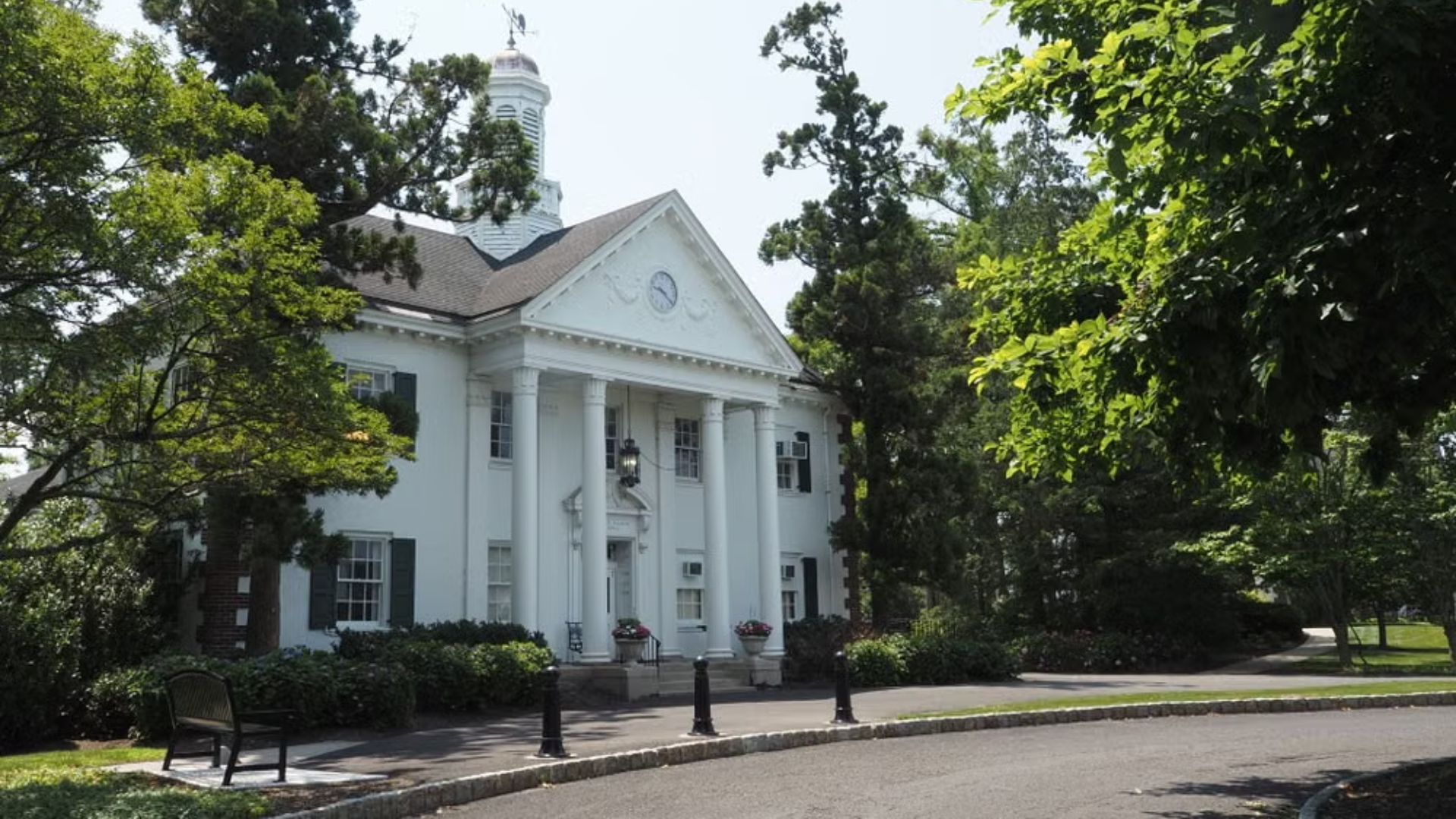 Exterior of a white, classical-style building with tall columns, a pediment clock, and a cupola.