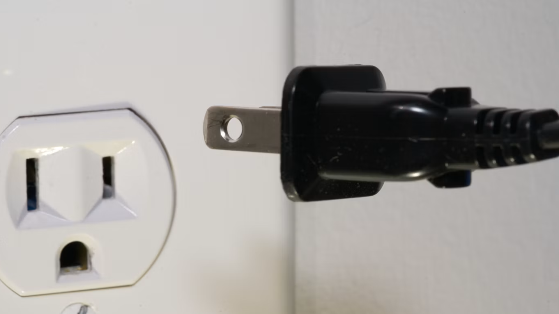 Close-up of a black electrical plug being inserted into a white wall outlet.