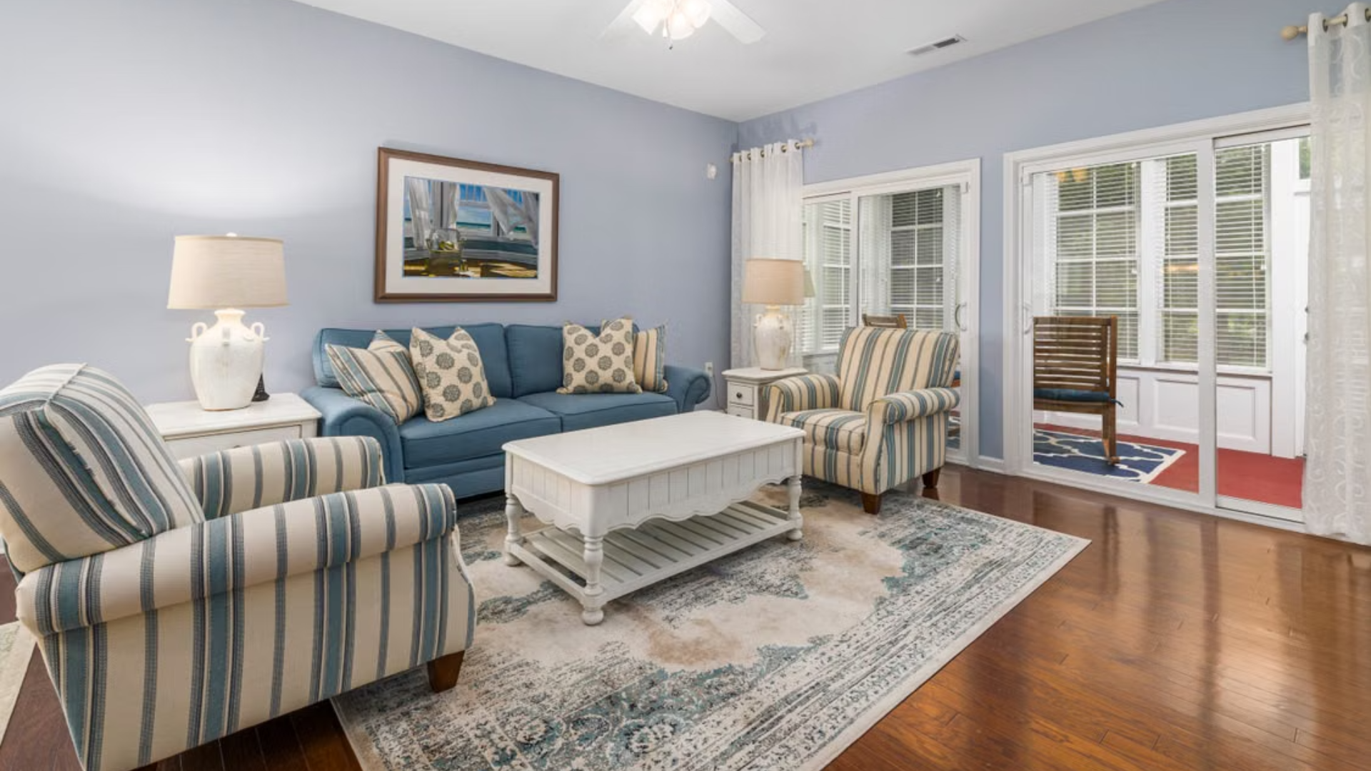 Living room featuring a blue sofa, striped armchairs, a white coffee table, and a sliding glass door.