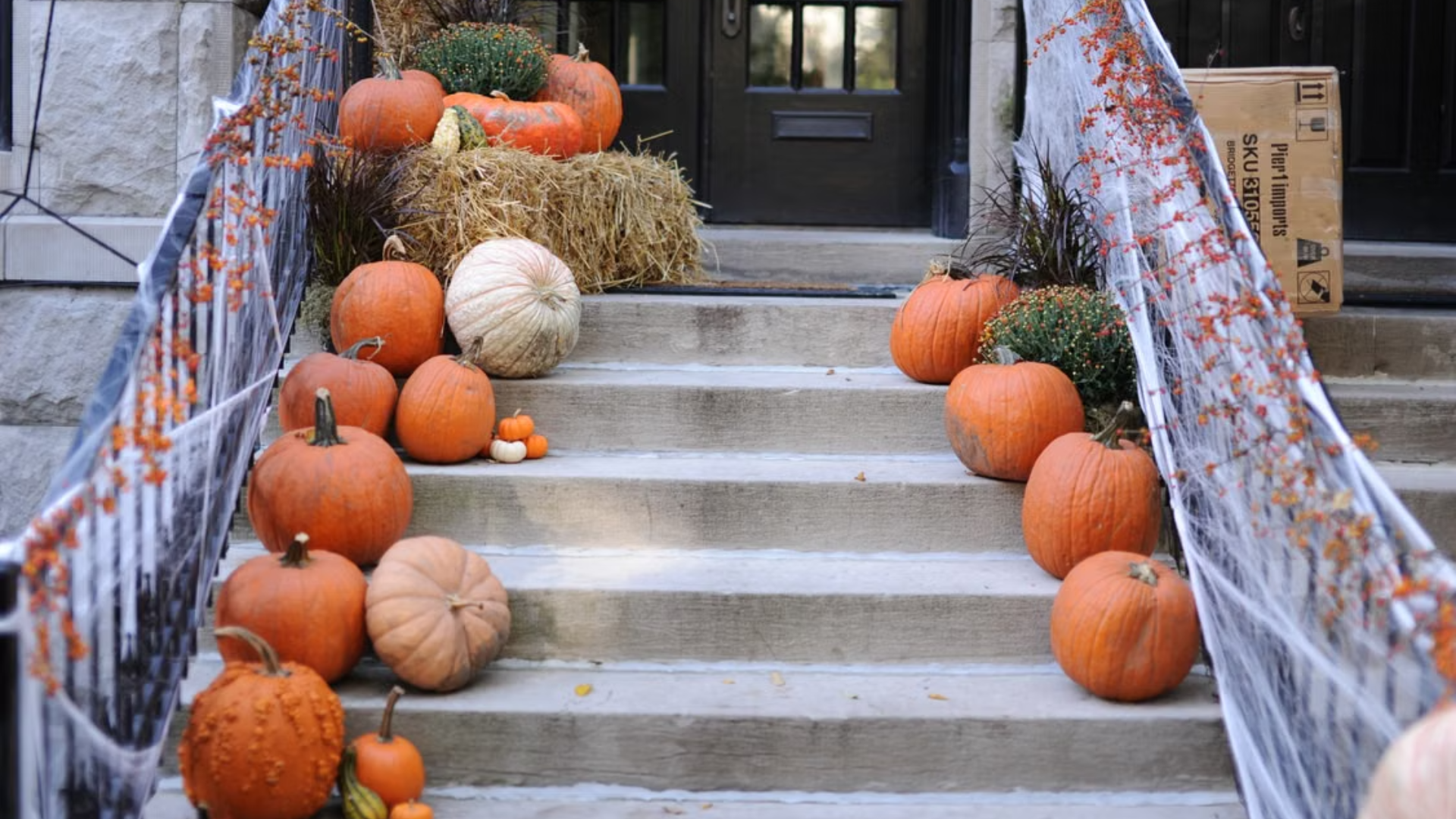 Front steps covered with pumpkins, a hay bale, and fake spiderwebs.