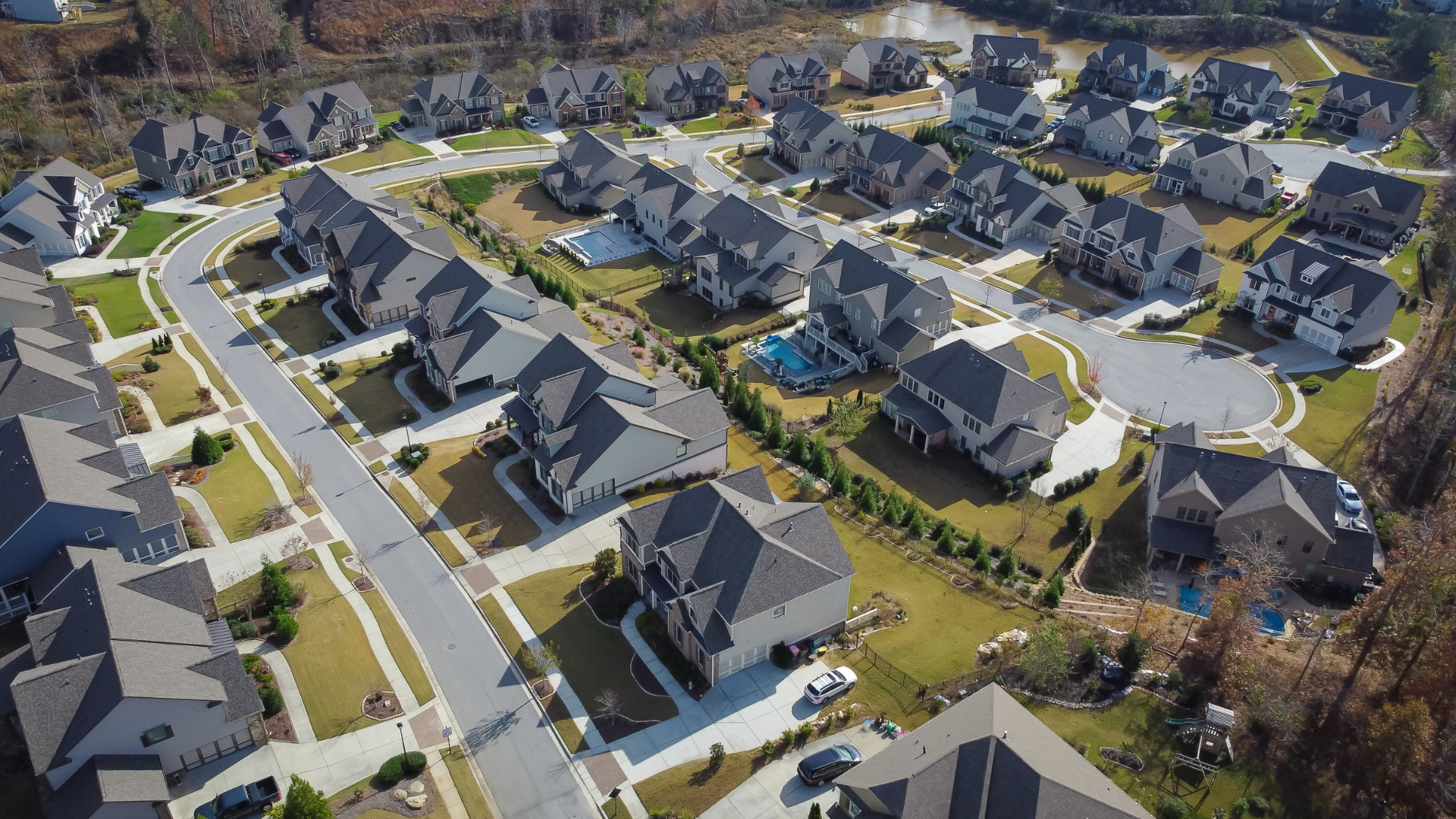 Aerial view of a suburban neighborhood featuring large houses, driveways, and backyard swimming pools.