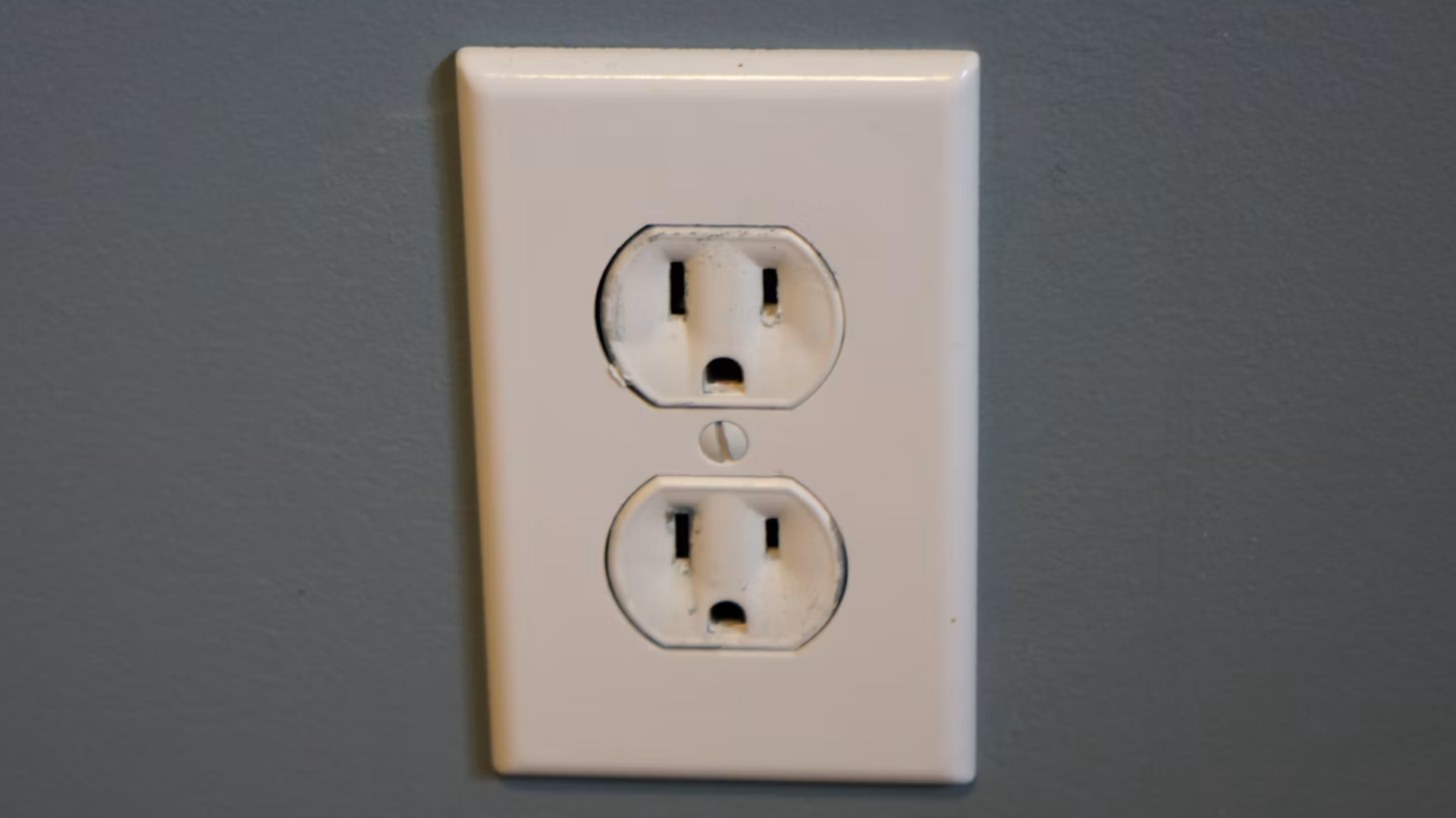 Close-up of a standard white double electrical outlet on a gray wall.