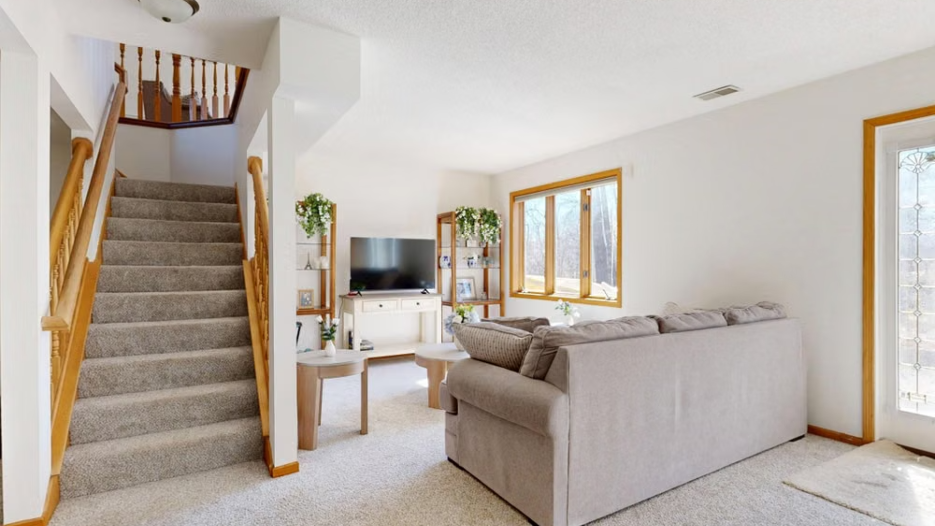 Living space with a gray sofa, a television on a console, and a carpeted staircase with a wooden handrail.