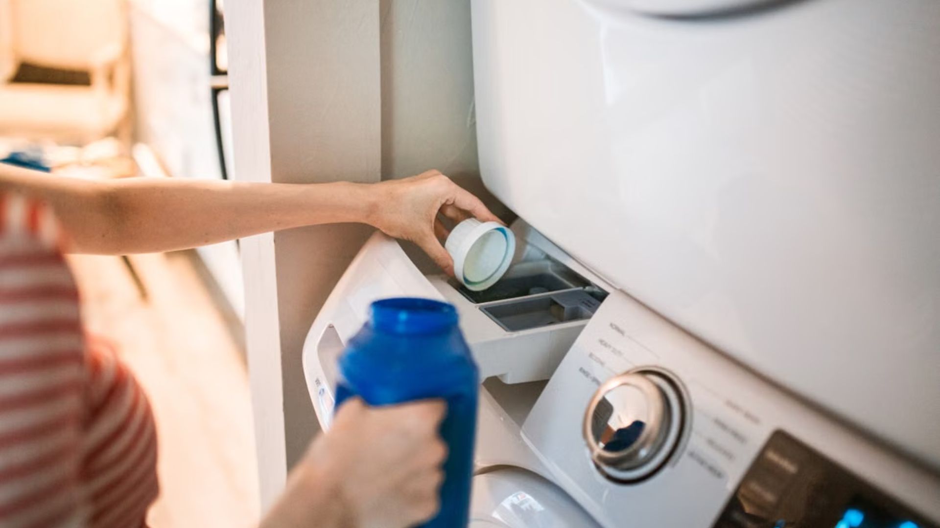 Close-up of a person pouring detergent into a front-loading washer.