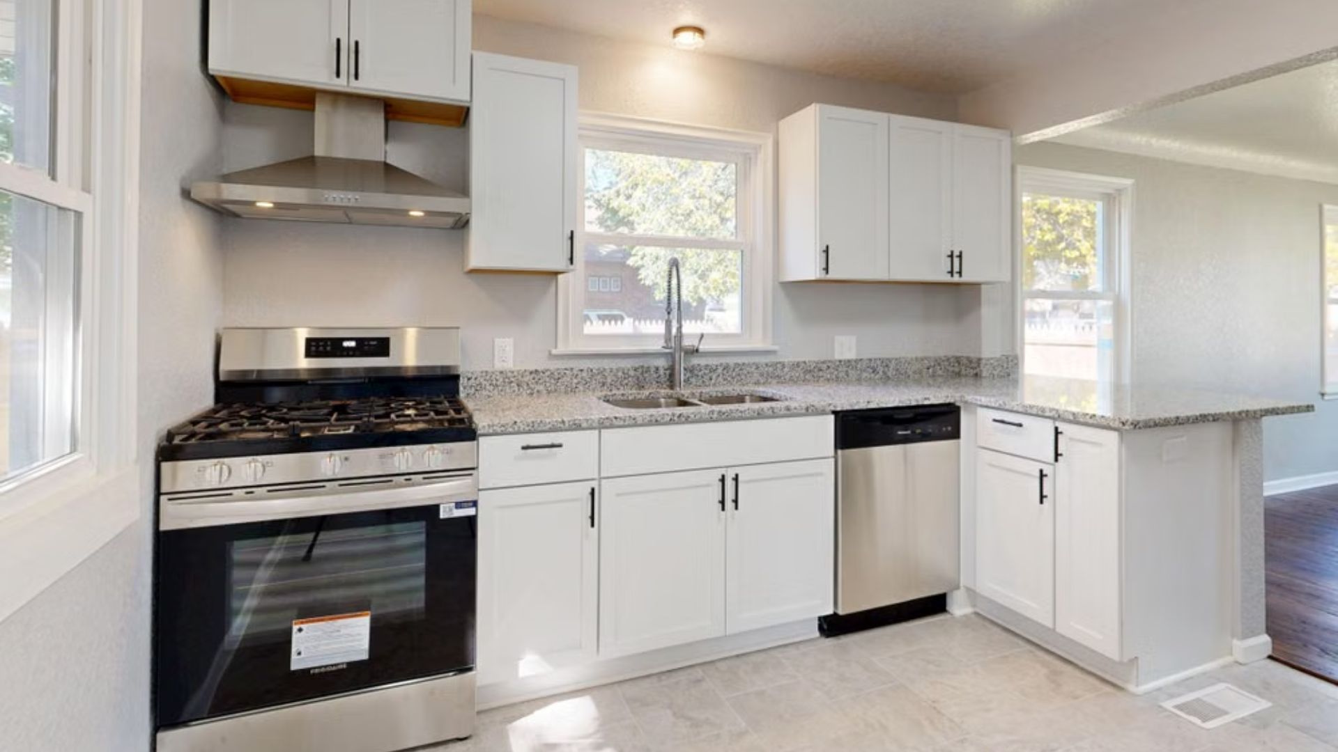 A bright, remodeled kitchen features white cabinetry, speckled granite countertops, and stainless steel appliances.