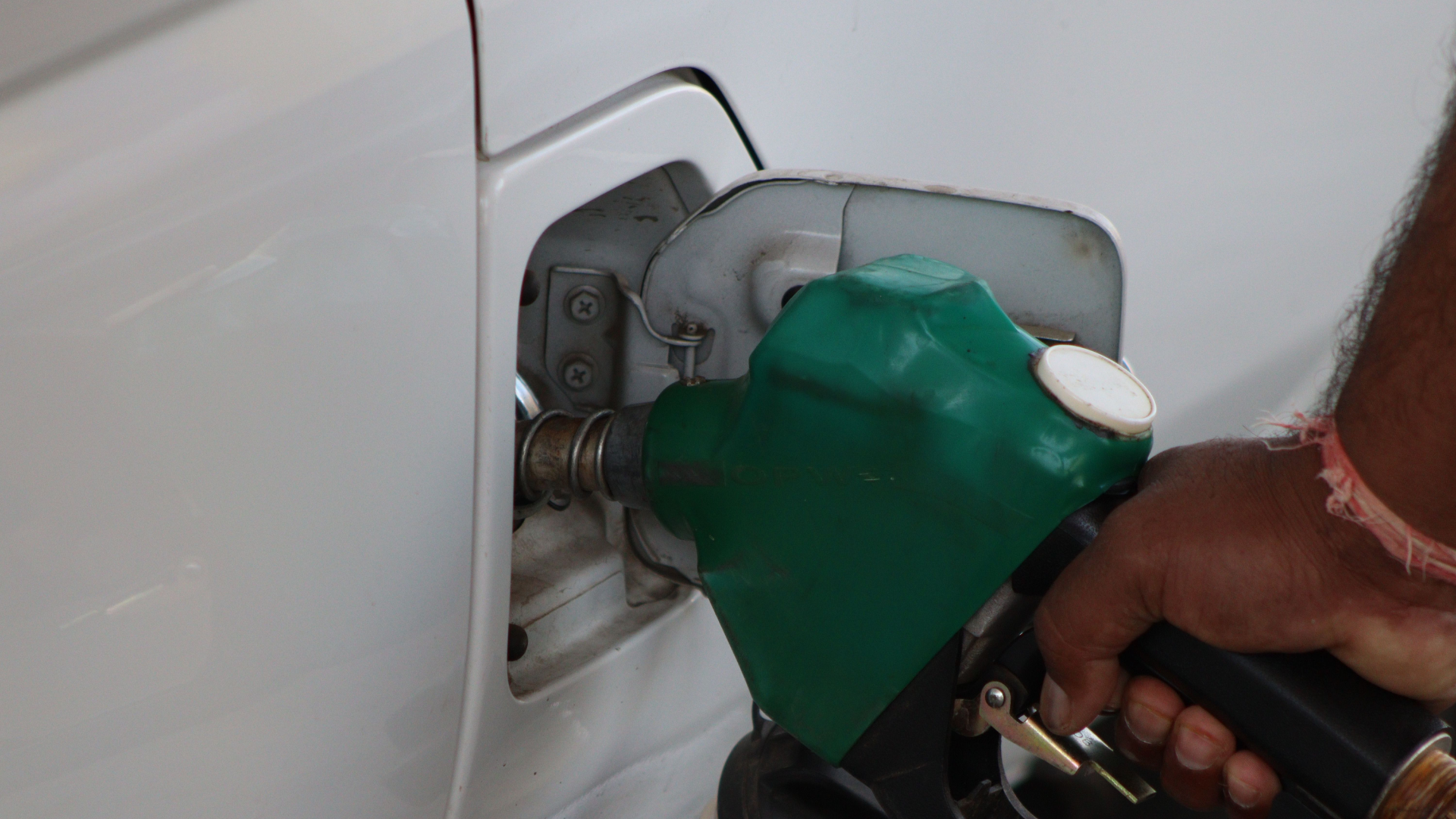 A close-up view of a green fuel nozzle inserted into a white car's gas tank during refueling.