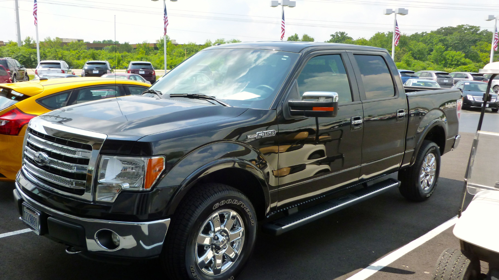 A glossy black Ford F-150 pickup truck parked outdoors in a dealership lot under sunny skies.
