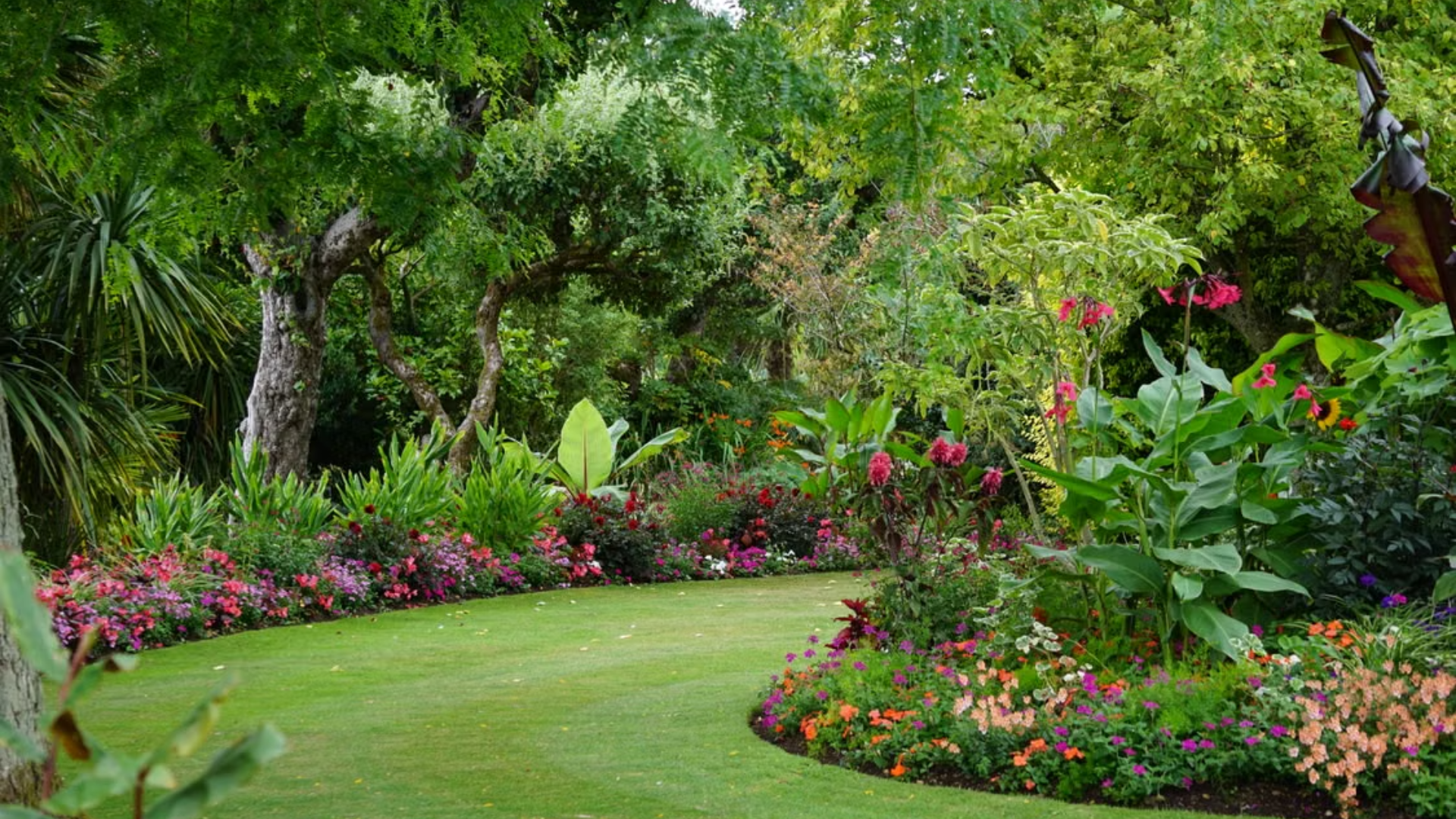  A lush garden path winds between vibrant flower beds and dense green trees.