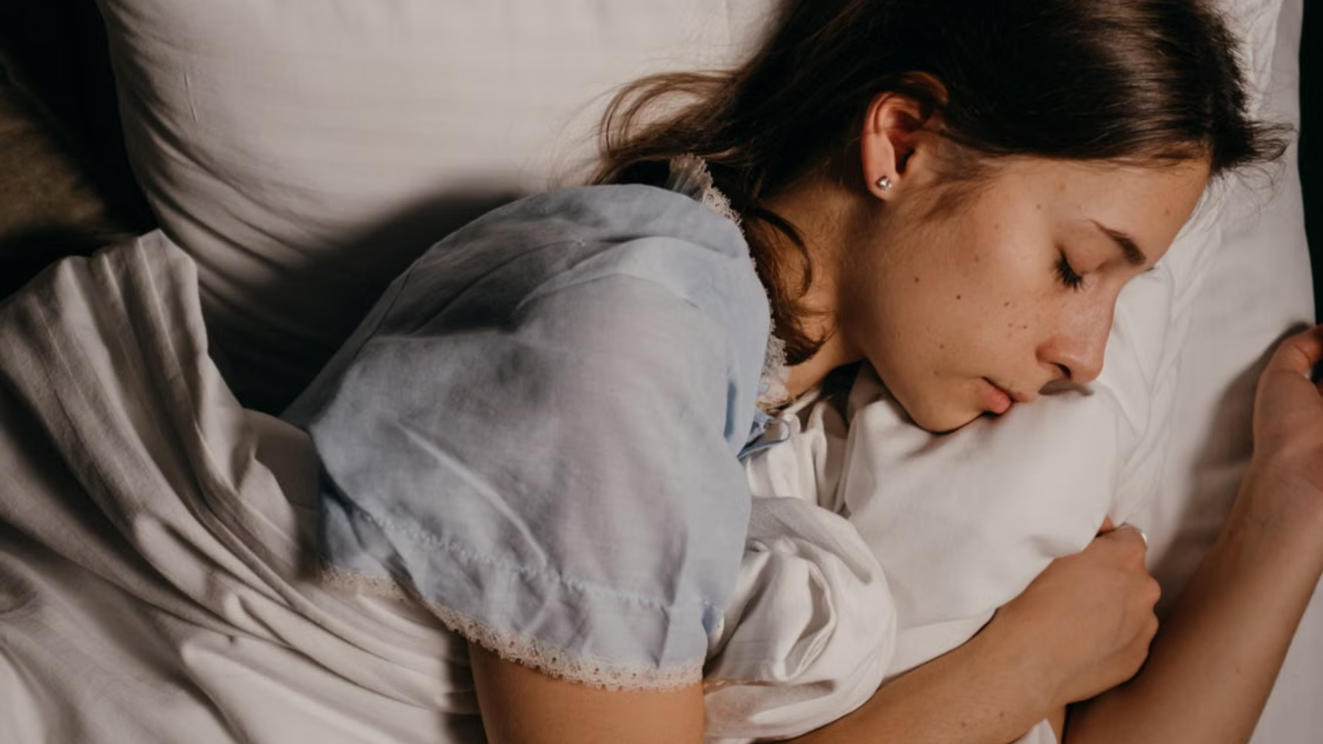 A young woman sleeps soundly on her side with her cheek resting against a white pillow.