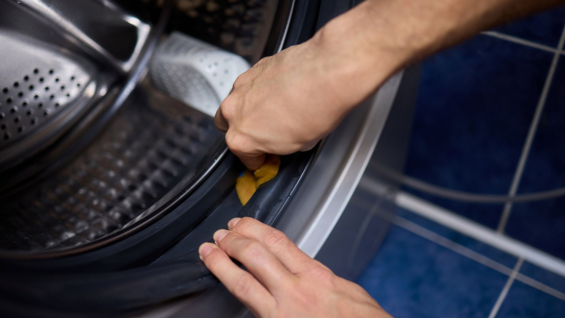 A detailed closeup view of hands thoroughly cleaning the rubber seal of a washing machine.