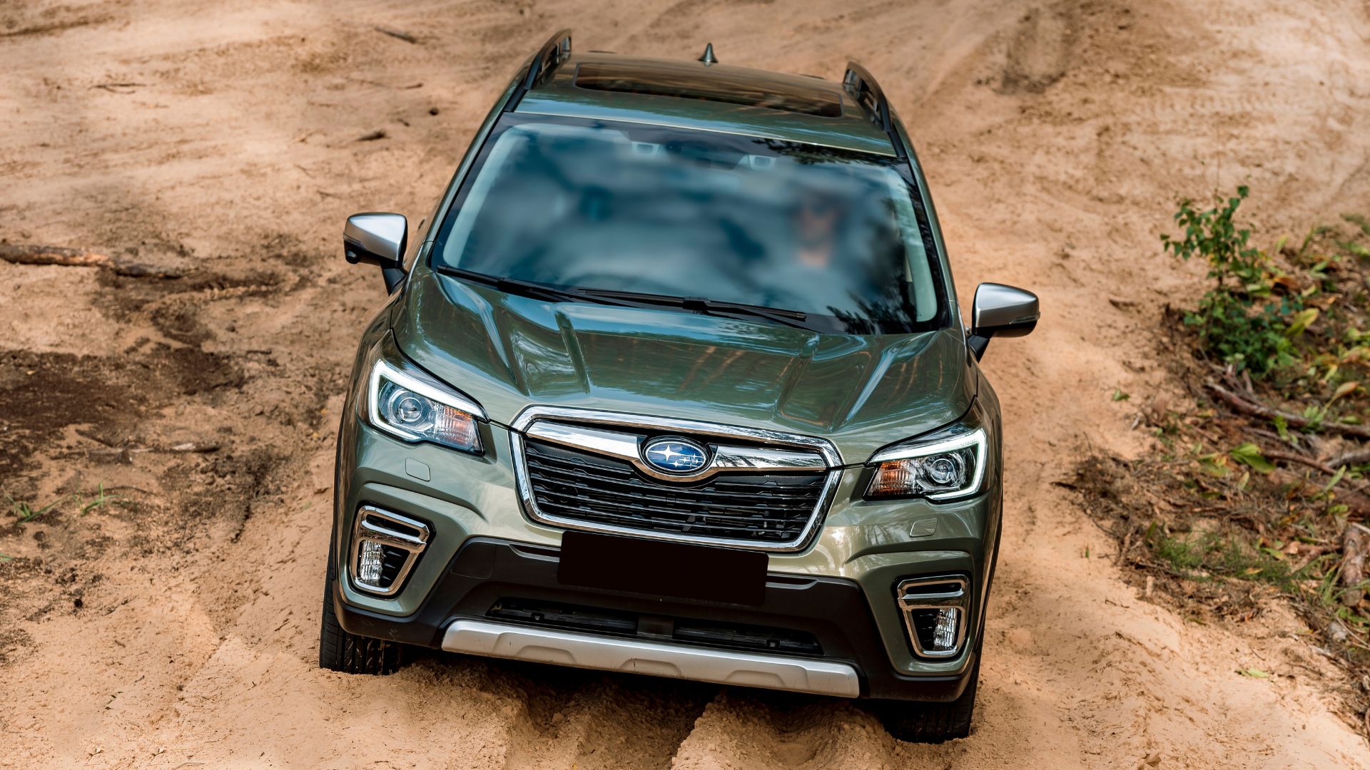 A green Subaru SUV drives through a sandy off-road trail.