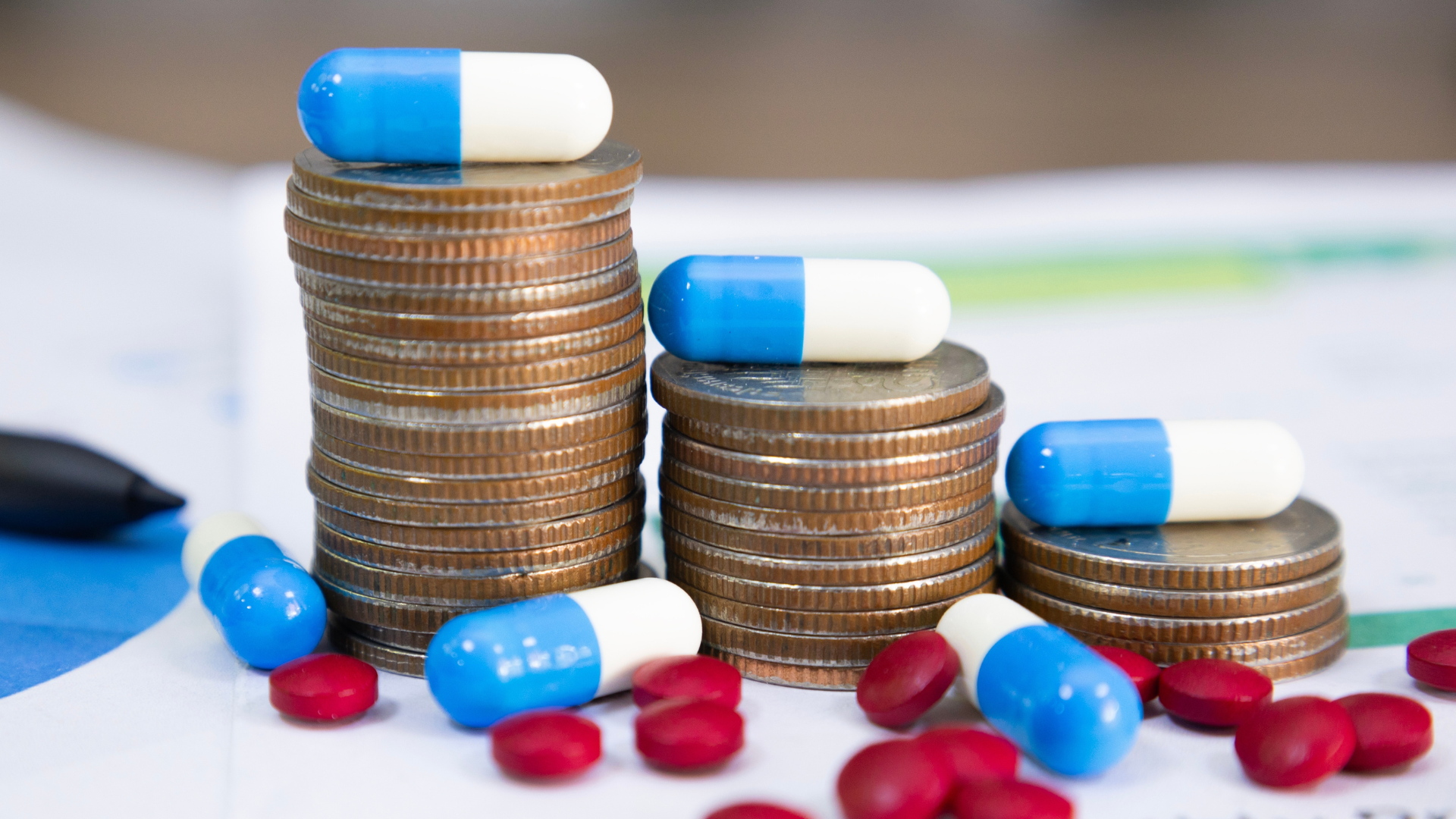 Blue and white capsules on a pile of coins and pills.