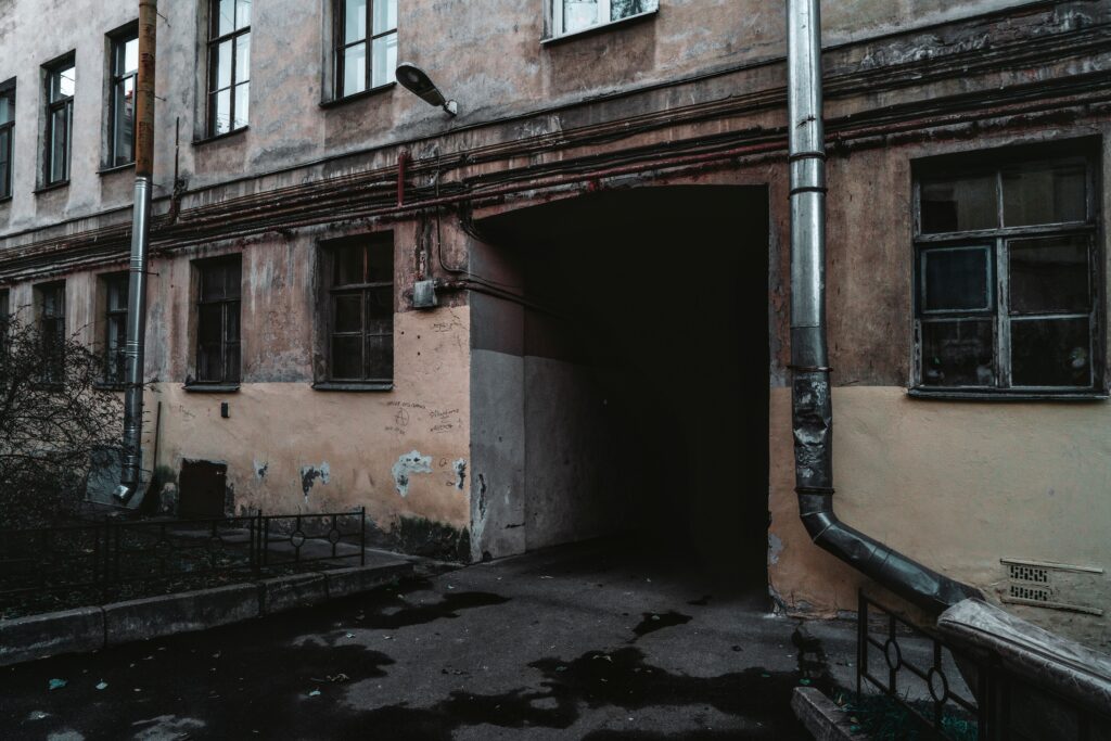 Weathered apartment building with exposed pipes and a dark entranceway.