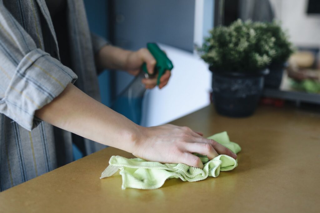 Person wiping a tabletop with a microfiber cloth and spray cleaner as part of a quick everyday cleaning routine.