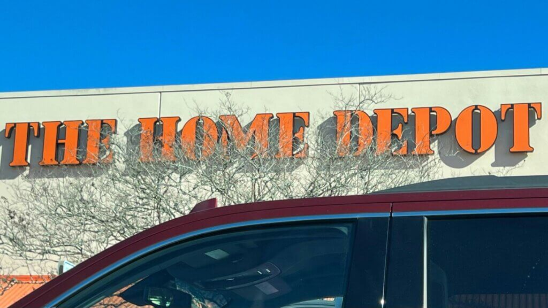 An exterior view of The Home Depot store logo mounted on the building facade above a parked car.