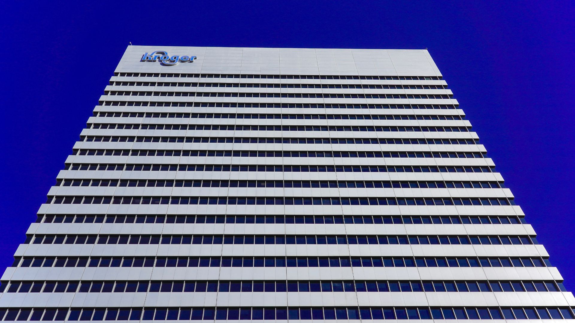 Tall Kroger corporate office building with rows of windows and the company logo against a deep blue sky.