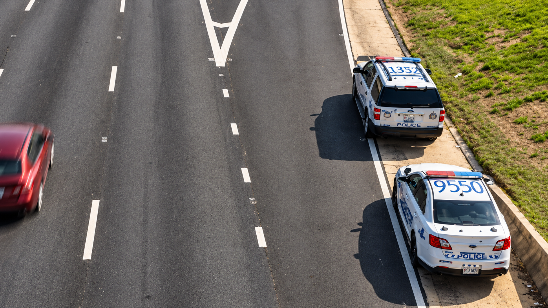 Aerial view of two police vehicles parked on the shoulder of a highway as a red car passes.