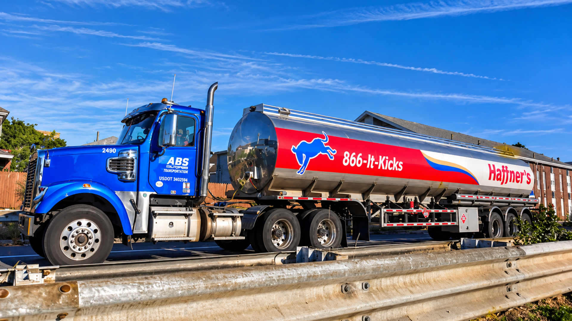 A blue ABS Transportation tanker truck driving along a road under a blue sky.