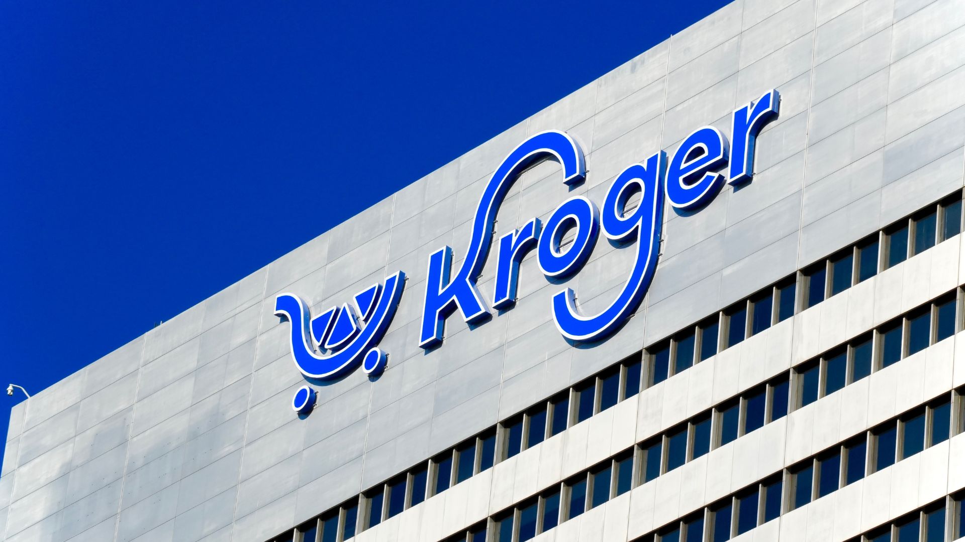 Large blue Kroger logo displayed on the upper facade of a modern office building beneath a clear blue sky.