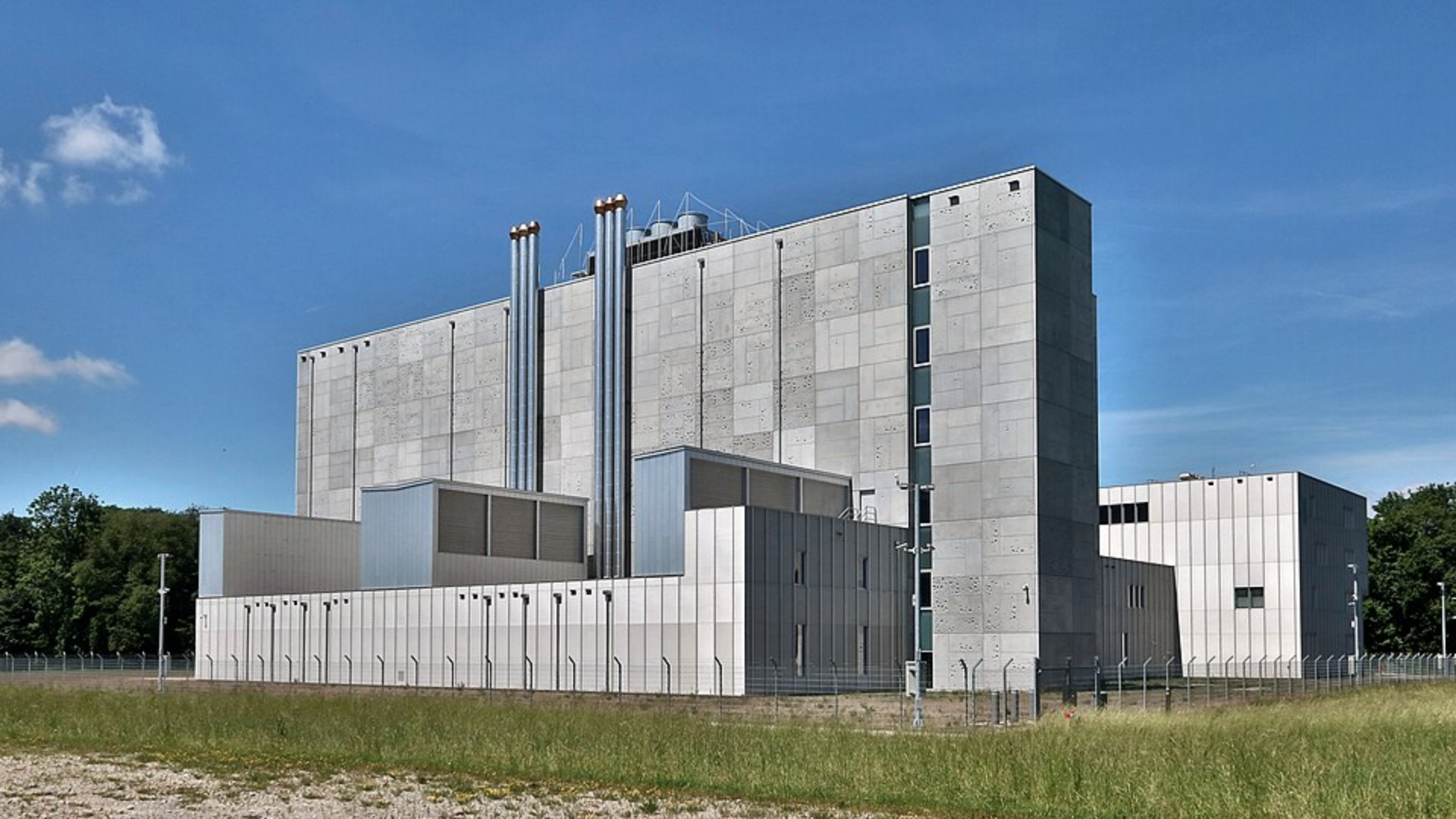A large, modern grey concrete AI data center with metal roof cooling stacks.