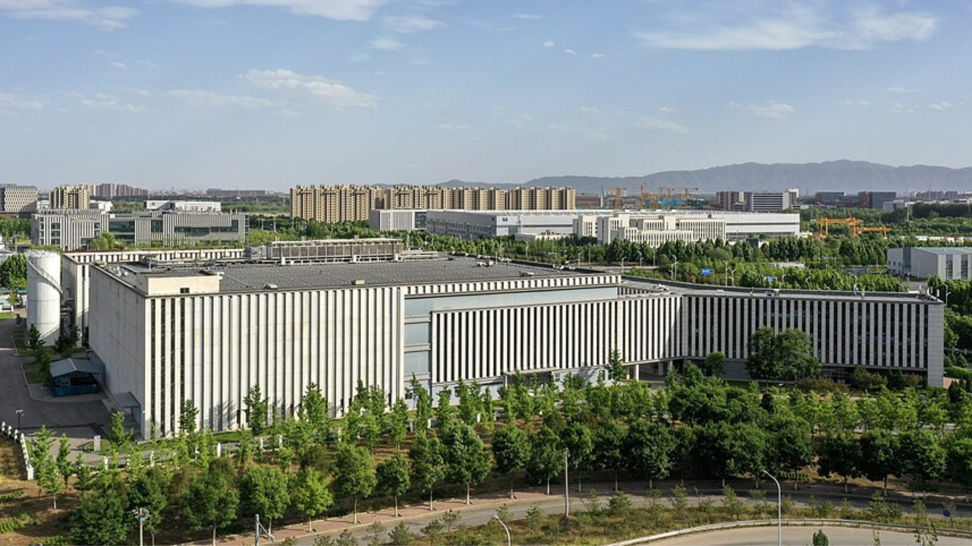 A sprawling AI data center complex surrounded by trees, with a city in the distance.