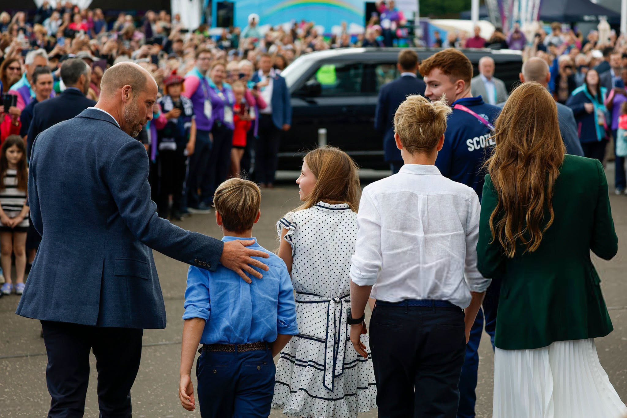 Prince William and Kate Middleton walk with their three children toward a crowd gathered at a public event.