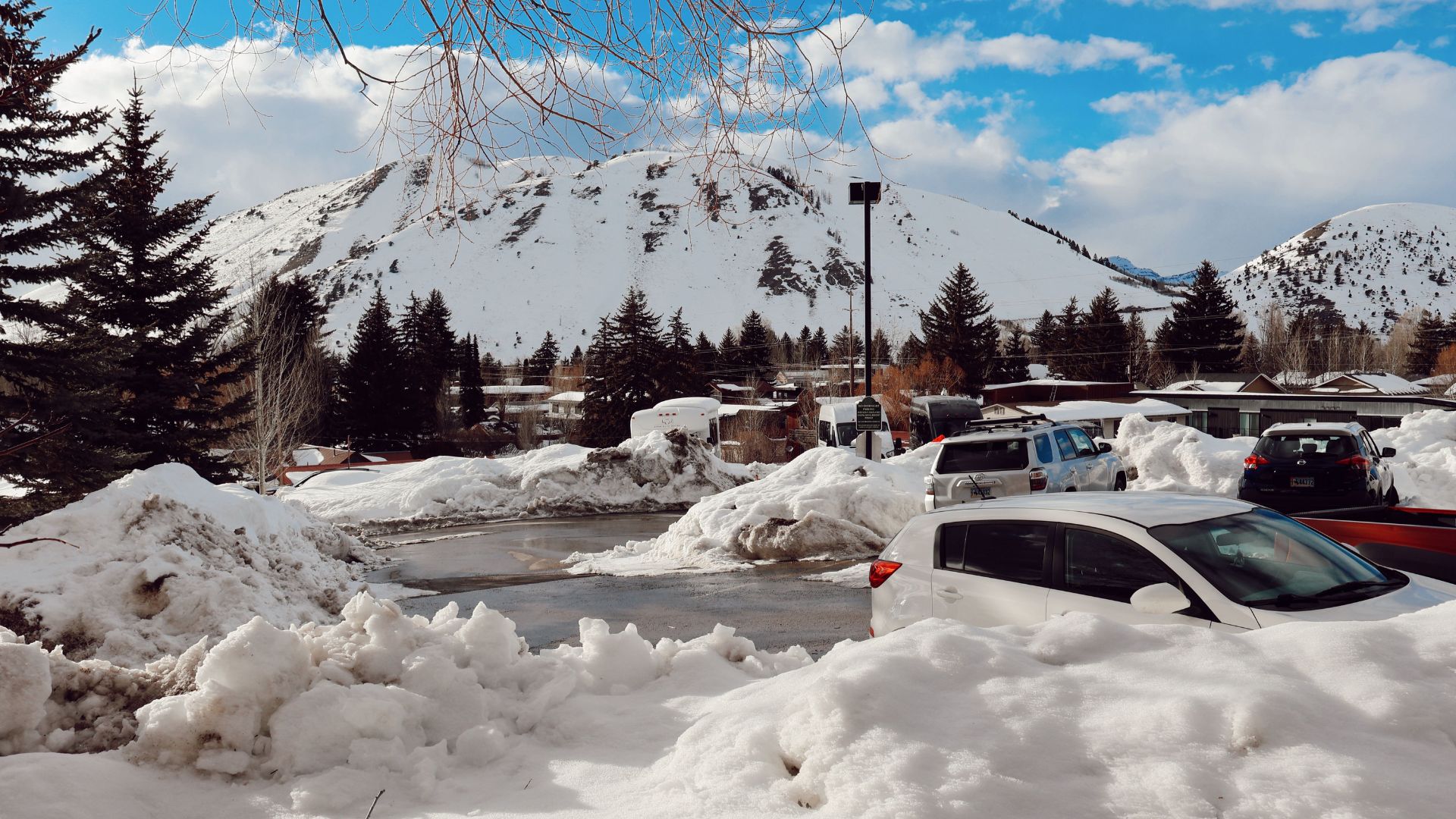 Snow-banked parking lot with parked cars and a snowy mountain behind.