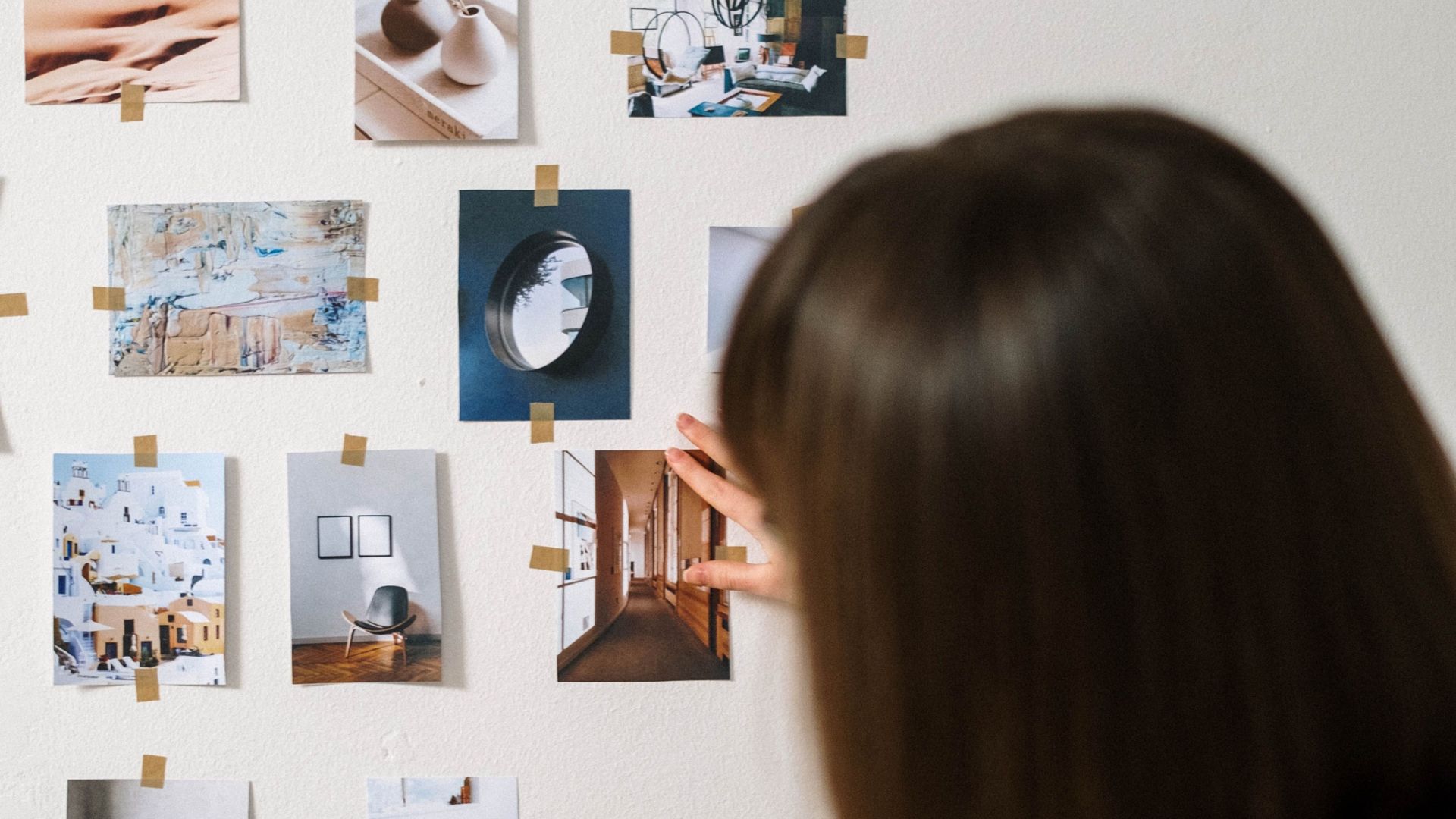 Woman arranging interior design and art inspiration photos on a wall.