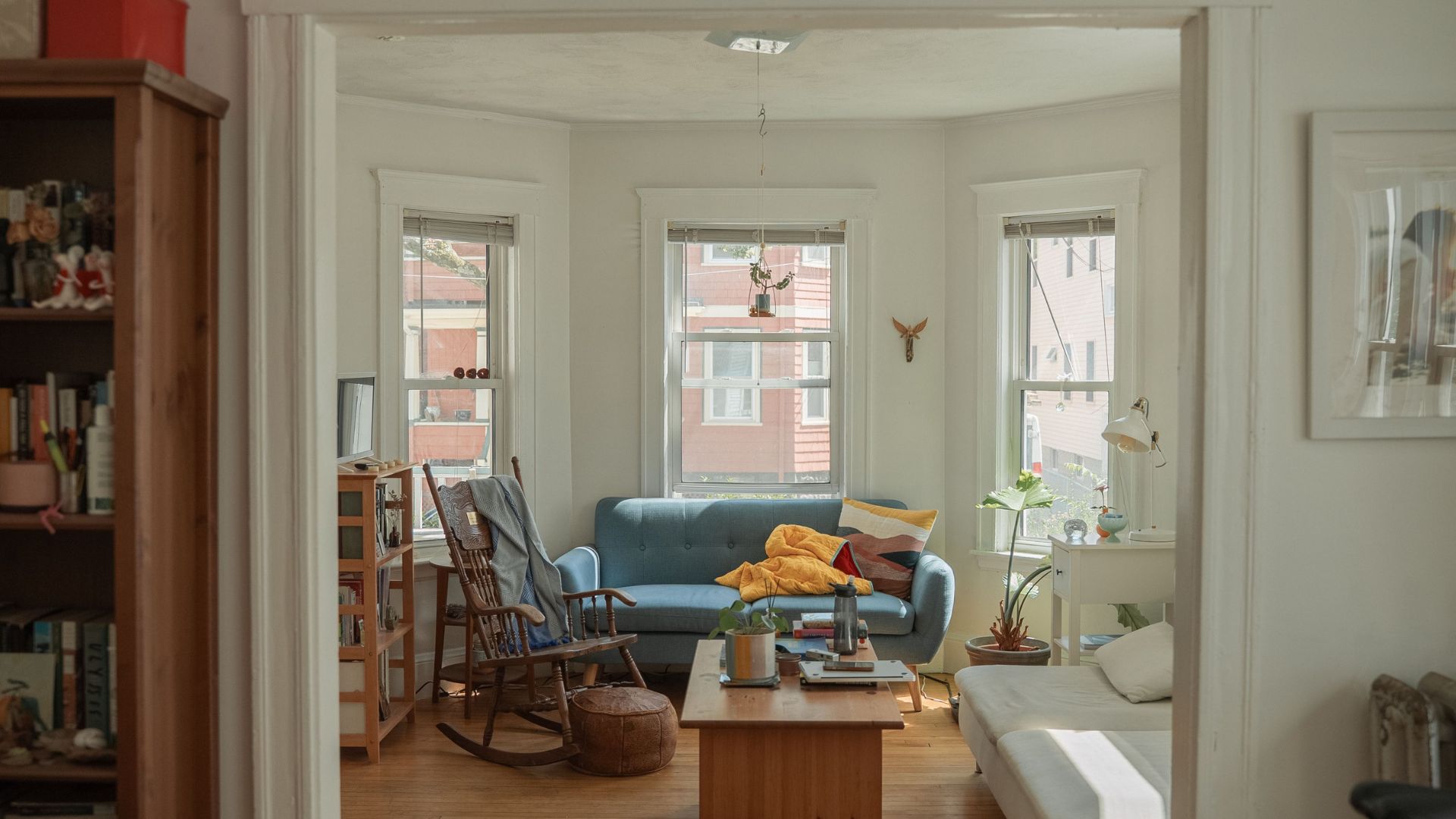 Bright living room with a blue sofa, wooden rocking chair, coffee table, and large windows.