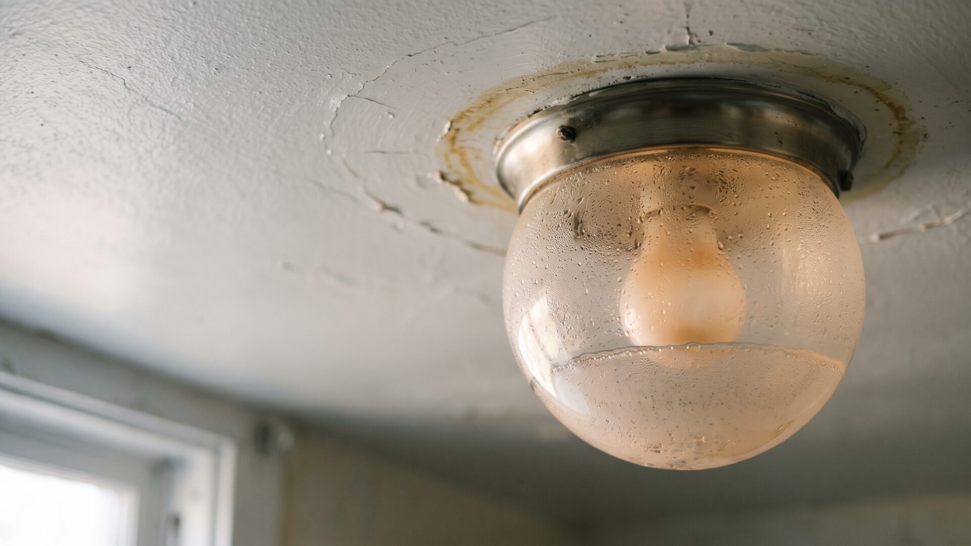 A single bathroom ceiling fixture with visible condensation fogging its glass dome, the exact failure condition slide 1 describes.